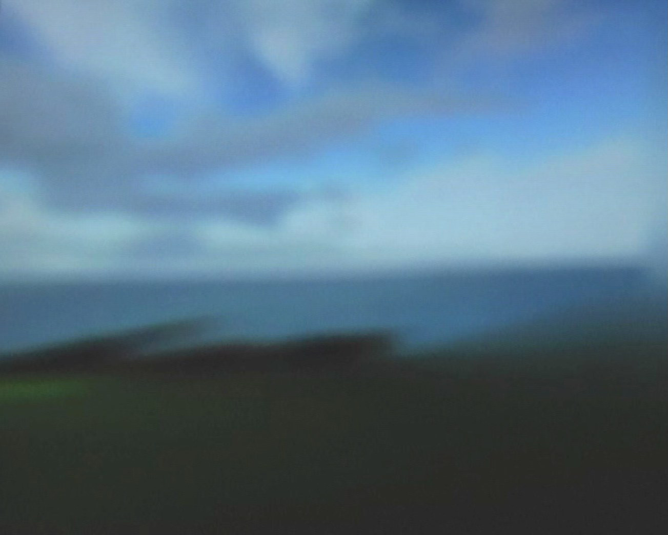 Photogramme flou du même paysage&nbsp;: les masses colorées ont perdu tout contour — le ciel bleu et gris se fond dans la mer, la ligne d'horizon devient incertaine, le talus n'est plus qu'une bande sombre. Un éclat de vert subsiste en bas à gauche. L'image tient dans le glissement des couleurs, comme un sfumato.