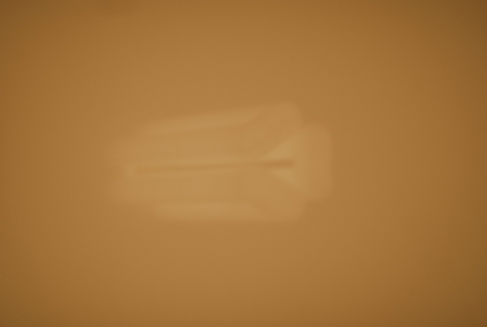 Un champ presque uni, ocre et ambré, traversé de dégradés lents, sans horizon ni repère. Au centre, légèrement décalée vers la gauche, une forme rectangulaire pâle flotte sans contour net&nbsp;: une clarté un peu plus jaune que le fond, qui se défait dans le grain de l'image.