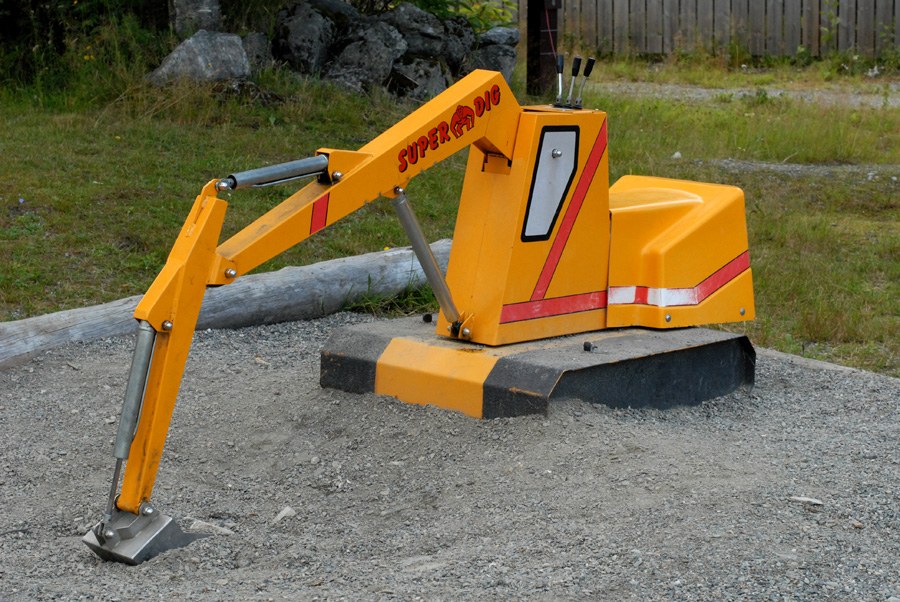 Pelleteuse de jeu jaune et rouge marquée « SUPER DIG », bras articulé abaissé et godet posé au sol, boulonnée sur un socle de béton, au milieu d'une aire de gravier.