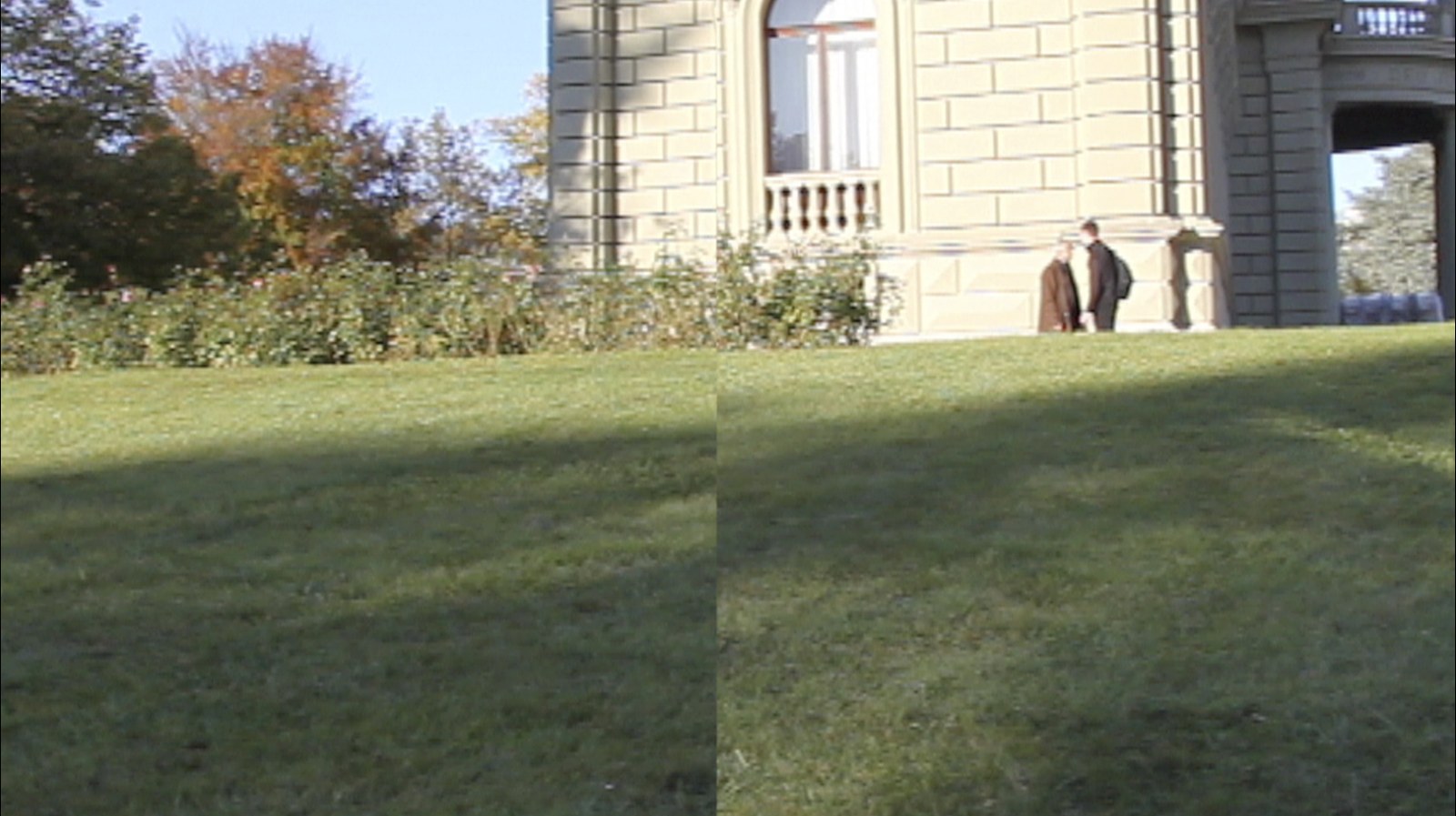 Premier état du panoramique&nbsp;: une pelouse en pente devant un hôtel particulier de pierre claire, dans une lumière de fin de journée. L'image est déjà partagée en deux moitiés légèrement décalées ; à droite, deux hommes en manteau discutent près de la façade. Au fond à gauche, des arbres aux feuillages d'automne.