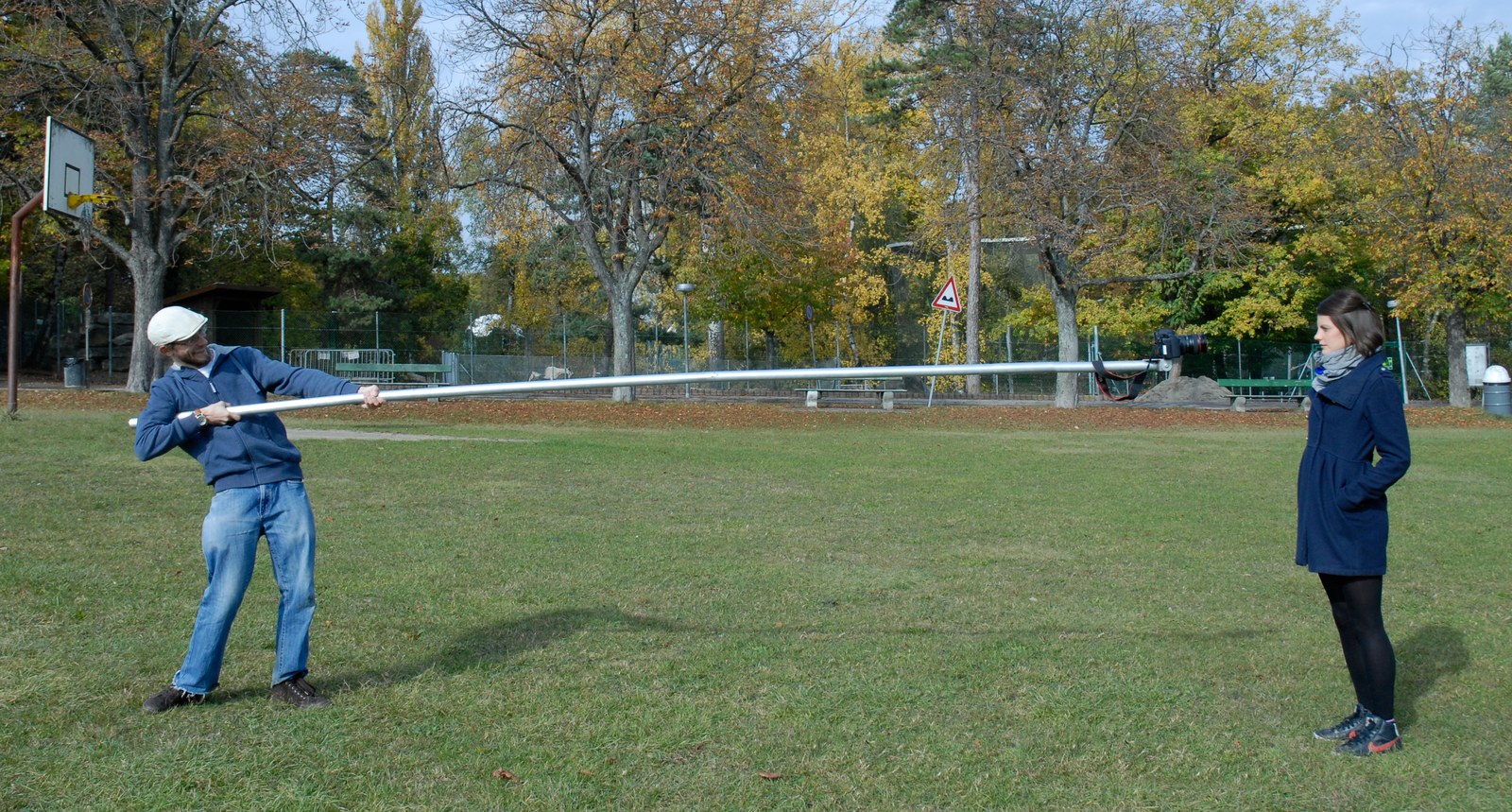 Le protocole, en extérieur : dans un parc en automne, un homme en sweat bleu tient à bout de bras une longue perche d'aluminium qui porte la caméra jusqu'au visage d'une femme en manteau bleu, debout à plusieurs mètres.
