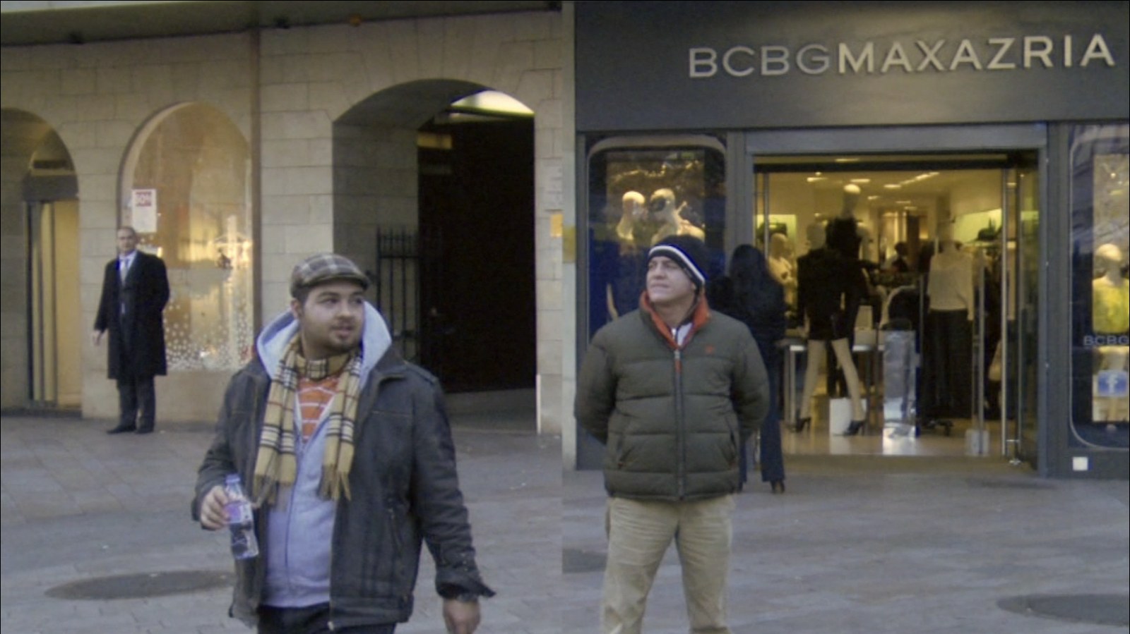 Photogramme&nbsp;: les deux moitiés se sont agrandies. À gauche, un homme au keffieh et à la casquette marche vers l'objectif, une bouteille à la main ; à droite, un homme au bonnet rayé se tient immobile devant l'entrée d'une boutique.