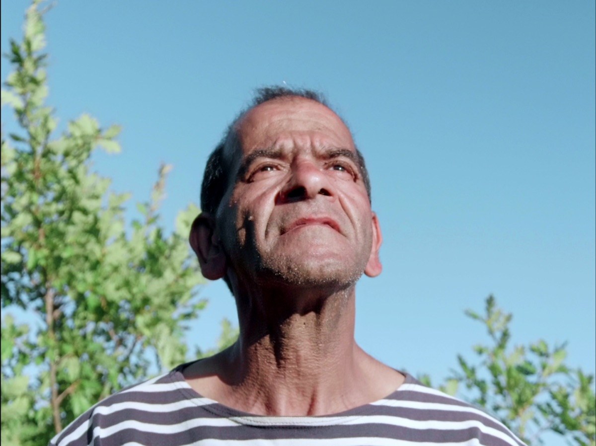 Photogramme : en contre-plongée sur un ciel bleu, le visage d'un homme en marinière, tête levée, les traits tendus.
