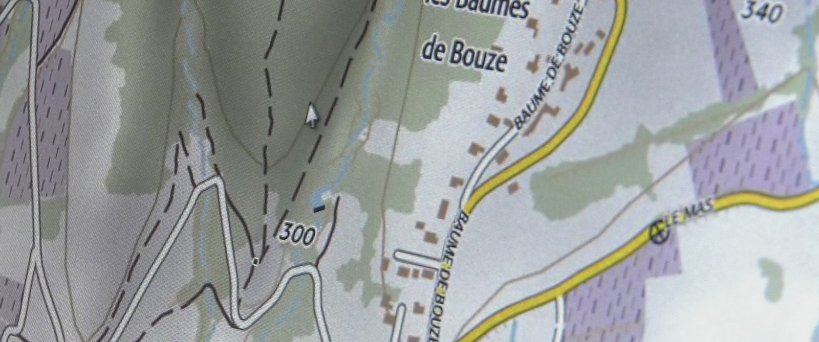 Photogramme : gros plan d'une carte topographique affichée à l'écran — courbes de niveau, hameaux, un curseur de souris posé au creux d'un vallon.